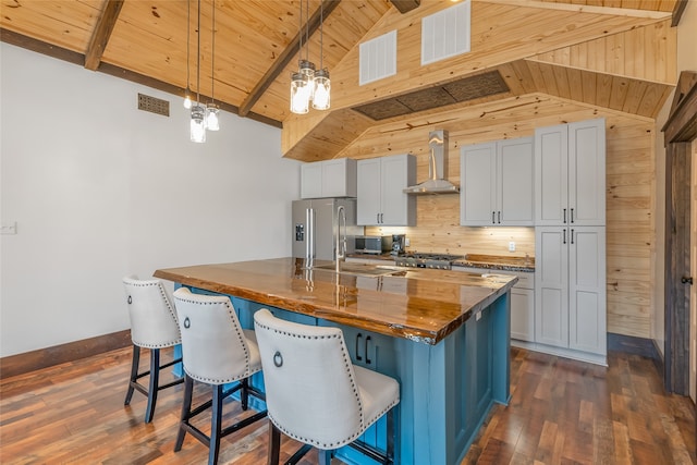 kitchen featuring a breakfast bar, pendant lighting, a kitchen island with sink, stainless steel appliances, and wall chimney exhaust hood