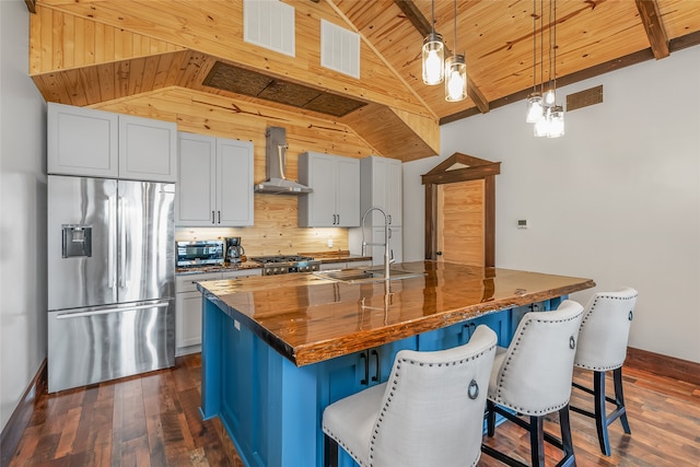 kitchen with stainless steel refrigerator with ice dispenser, a breakfast bar, a center island with sink, and wall chimney exhaust hood