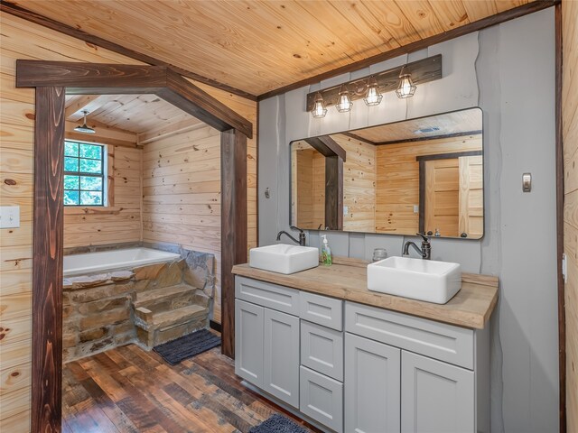 bathroom with hardwood / wood-style floors, wood walls, tiled bath, vanity, and wooden ceiling