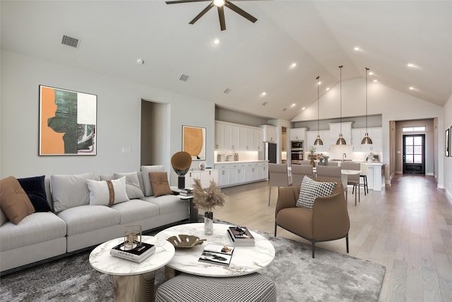 living room with ceiling fan, high vaulted ceiling, and light hardwood / wood-style floors