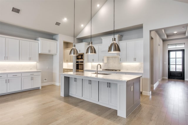 kitchen featuring appliances with stainless steel finishes, sink, a center island with sink, white cabinets, and hanging light fixtures