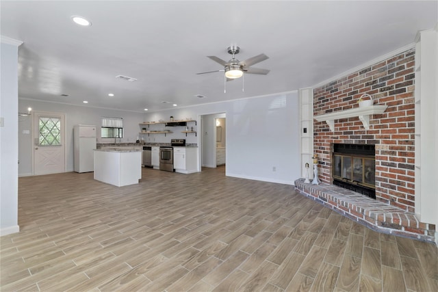 unfurnished living room with ornamental molding, ceiling fan, light wood-type flooring, and a brick fireplace