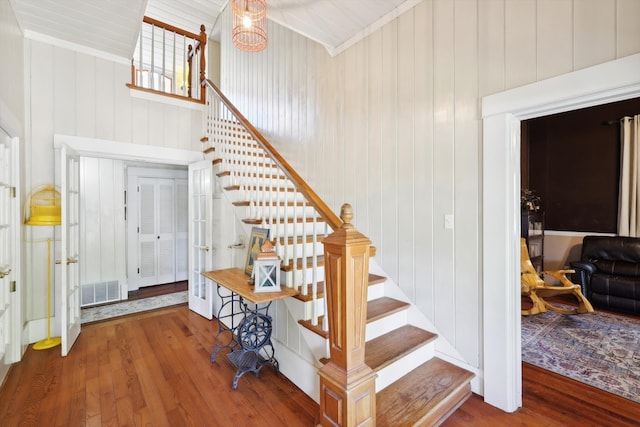 stairs with ornamental molding, hardwood / wood-style floors, wooden walls, and a high ceiling