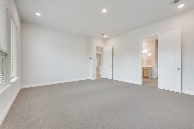 unfurnished bedroom featuring light colored carpet and ensuite bathroom