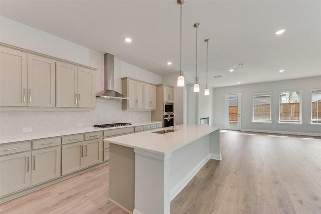 kitchen featuring sink, light wood-type flooring, wall chimney range hood, and hanging light fixtures