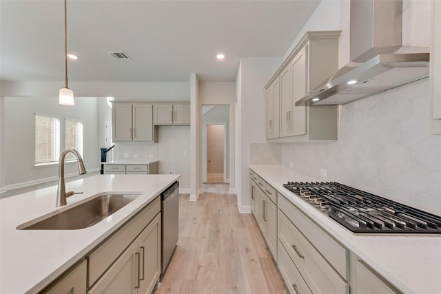 kitchen featuring appliances with stainless steel finishes, wall chimney exhaust hood, sink, pendant lighting, and light hardwood / wood-style flooring