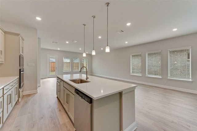 kitchen with a center island with sink, hanging light fixtures, sink, light wood-type flooring, and appliances with stainless steel finishes