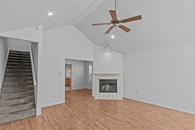 unfurnished living room with a fireplace, light hardwood / wood-style flooring, a textured ceiling, high vaulted ceiling, and ceiling fan