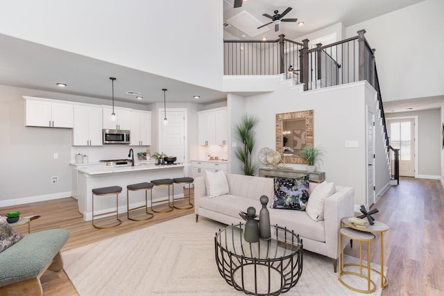 living room featuring a high ceiling, light hardwood / wood-style flooring, ceiling fan, and sink