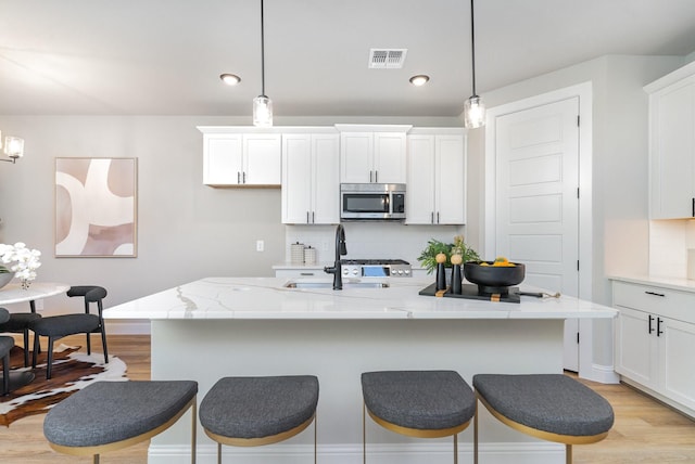 kitchen featuring decorative light fixtures, sink, an island with sink, and tasteful backsplash