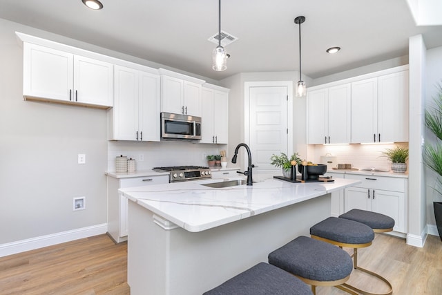 kitchen featuring white cabinets, stainless steel appliances, a kitchen island with sink, and sink