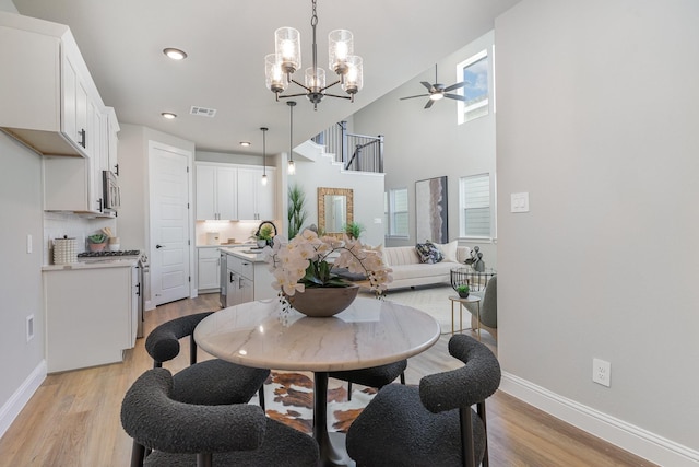 dining area featuring ceiling fan with notable chandelier, a towering ceiling, sink, and light hardwood / wood-style flooring