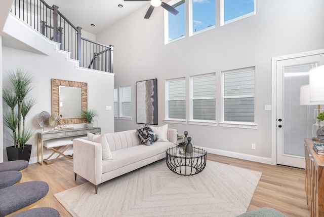 living room featuring ceiling fan, light wood-type flooring, and a towering ceiling