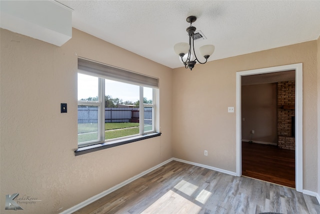 unfurnished room with an inviting chandelier, a textured ceiling, and light hardwood / wood-style floors