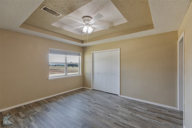 unfurnished bedroom with a closet, hardwood / wood-style floors, a raised ceiling, and ceiling fan