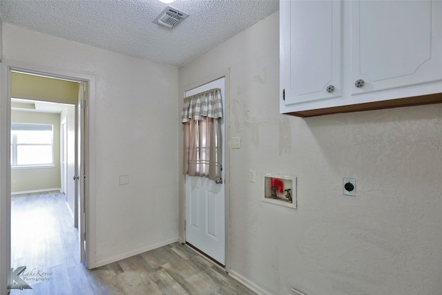 laundry area featuring electric dryer hookup, washer hookup, cabinets, a textured ceiling, and light hardwood / wood-style floors