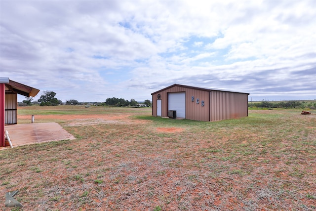 view of yard featuring a rural view, an outdoor structure, a garage, and cooling unit