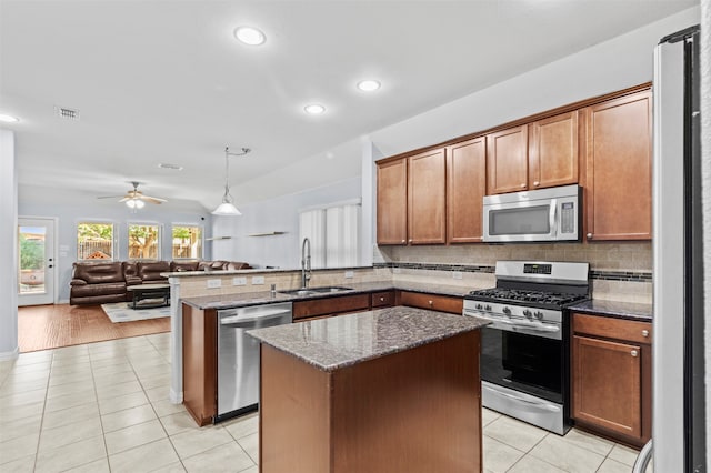 kitchen featuring kitchen peninsula, appliances with stainless steel finishes, dark stone counters, light hardwood / wood-style flooring, and sink