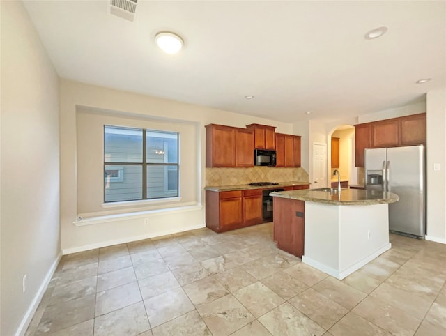 kitchen with an island with sink, stainless steel refrigerator with ice dispenser, backsplash, sink, and range with gas cooktop