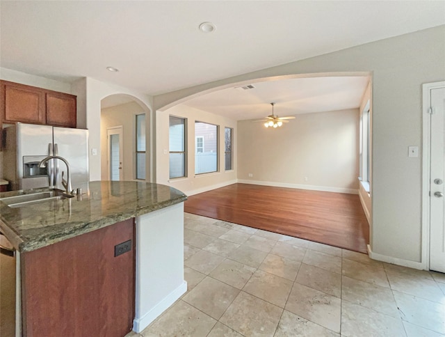 kitchen featuring sink, ceiling fan, light hardwood / wood-style floors, dark stone counters, and stainless steel refrigerator with ice dispenser