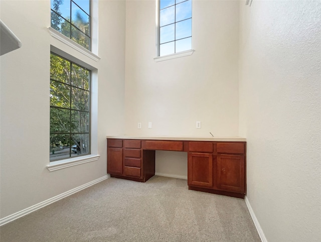 unfurnished office featuring built in desk, light colored carpet, and a towering ceiling