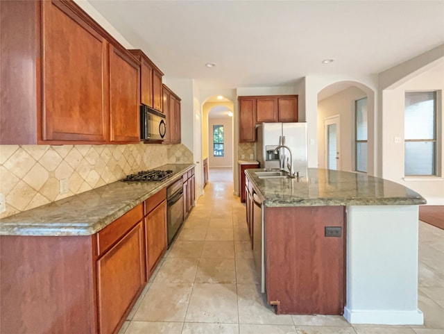 kitchen with an island with sink, backsplash, sink, stone counters, and appliances with stainless steel finishes