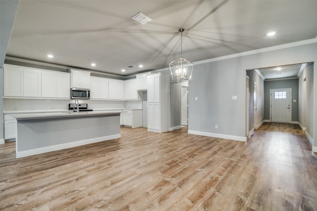 kitchen with white cabinets, hanging light fixtures, a kitchen island with sink, and light wood-type flooring