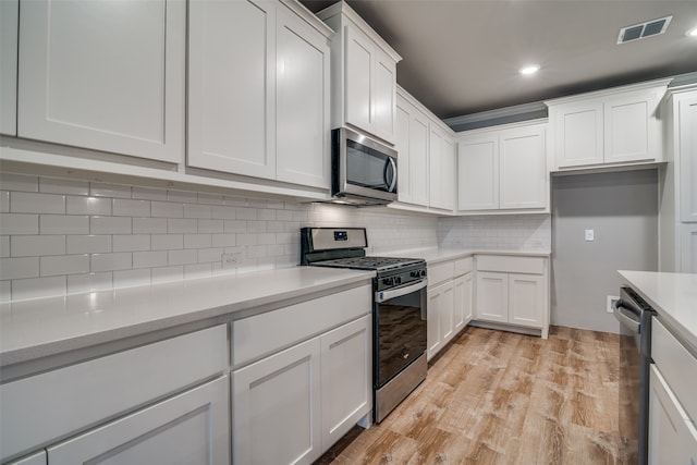 kitchen with backsplash, white cabinets, light wood-type flooring, appliances with stainless steel finishes, and light stone counters