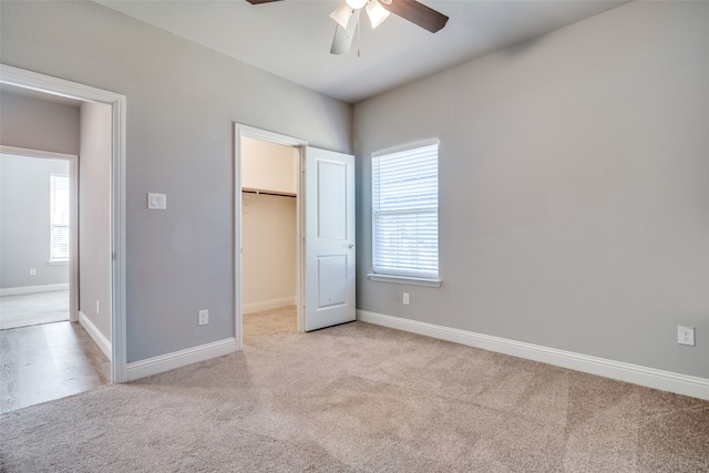 unfurnished bedroom featuring a spacious closet, light colored carpet, a closet, and ceiling fan