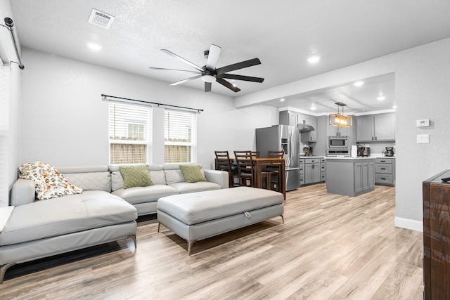 living room featuring a textured ceiling, light hardwood / wood-style floors, and ceiling fan