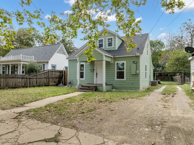 bungalow-style home featuring fence, roof with shingles, a front lawn, dirt driveway, and cooling unit