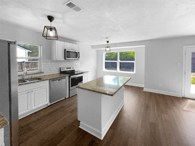 kitchen featuring appliances with stainless steel finishes, a kitchen island, white cabinetry, pendant lighting, and dark hardwood / wood-style floors