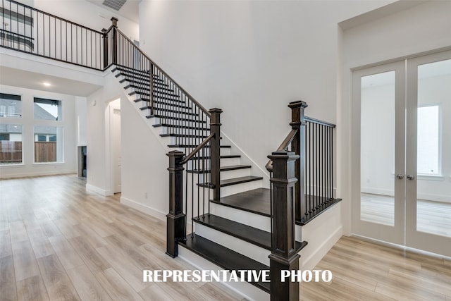 staircase with a towering ceiling, french doors, and hardwood / wood-style flooring