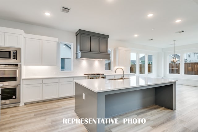 kitchen featuring white cabinetry, light wood-type flooring, sink, and an island with sink