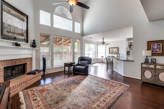 living room featuring a towering ceiling, dark hardwood / wood-style floors, a fireplace, and ceiling fan