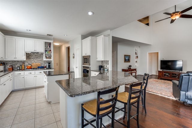 kitchen featuring a center island, stainless steel appliances, dark stone counters, white cabinets, and light hardwood / wood-style flooring