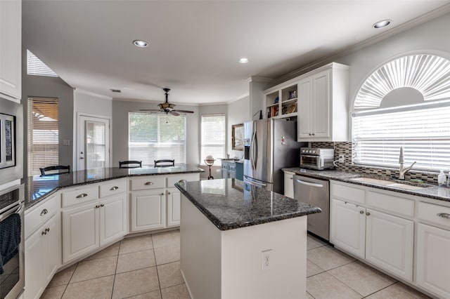 kitchen with appliances with stainless steel finishes, sink, a kitchen island, white cabinetry, and dark stone counters