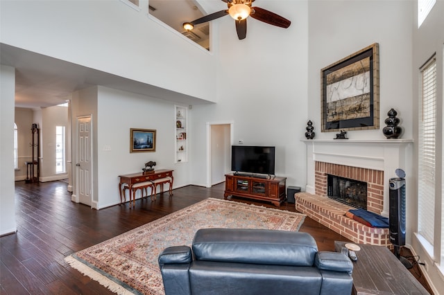 living room with a high ceiling, ceiling fan, dark wood-type flooring, and a brick fireplace