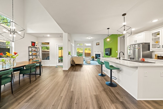 kitchen with stainless steel fridge, white cabinets, hanging light fixtures, dark hardwood / wood-style flooring, and a kitchen breakfast bar