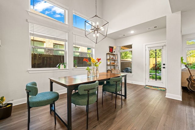 dining room with dark wood-type flooring, an inviting chandelier, plenty of natural light, and a high ceiling