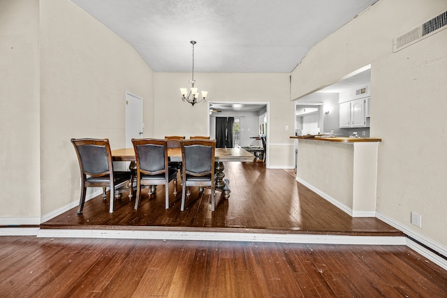 dining space with a notable chandelier, wood-type flooring, and vaulted ceiling