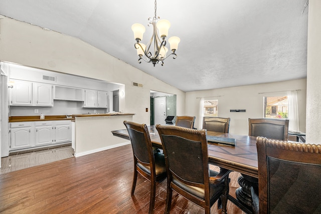 dining space with dark wood-type flooring, a notable chandelier, a textured ceiling, and vaulted ceiling