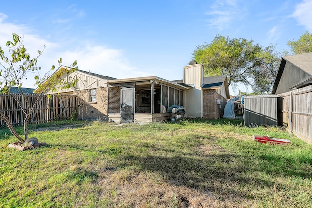 rear view of property featuring a shed, a yard, and a sunroom