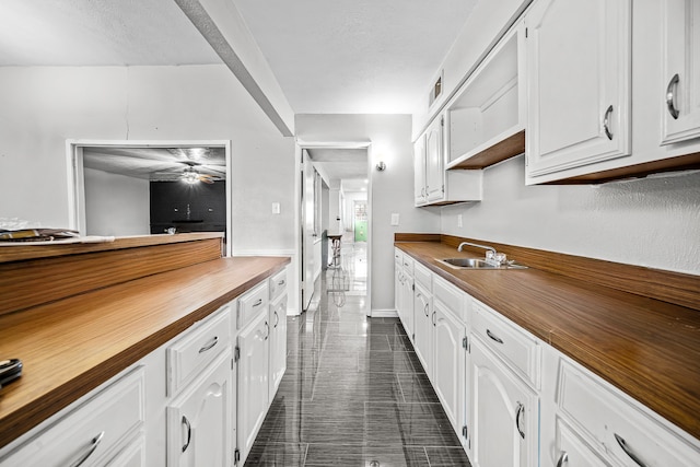 kitchen featuring butcher block countertops, sink, white cabinets, and ceiling fan