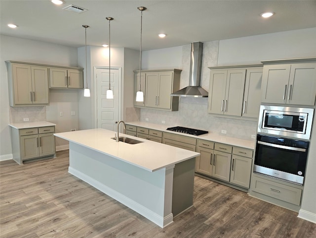 kitchen featuring decorative backsplash, hardwood / wood-style flooring, wall chimney exhaust hood, stainless steel appliances, and sink