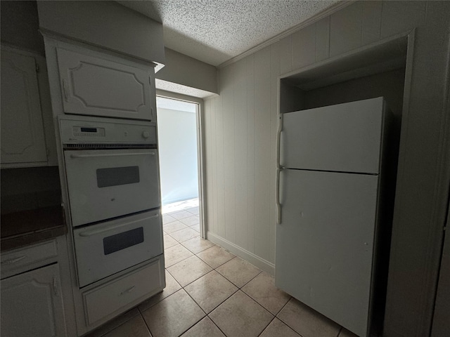 kitchen featuring light tile patterned floors, white cabinetry, a textured ceiling, ornamental molding, and white appliances