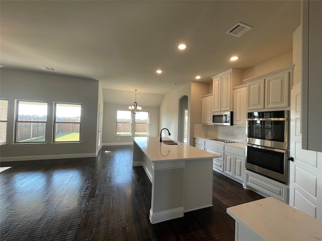 kitchen with tasteful backsplash, appliances with stainless steel finishes, sink, a chandelier, and a center island with sink