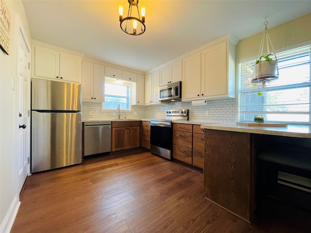 kitchen featuring dark wood-type flooring, decorative light fixtures, stainless steel appliances, and tasteful backsplash