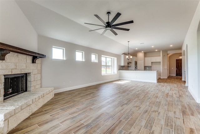 unfurnished living room featuring ceiling fan with notable chandelier, lofted ceiling, light hardwood / wood-style flooring, and a fireplace