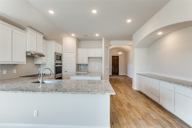 kitchen with stainless steel appliances, sink, light wood-type flooring, white cabinetry, and light stone counters